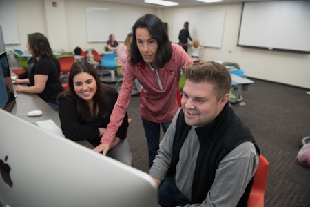 Professor assisting communication students while in a communications computer lab classroom