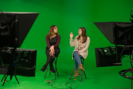 Two school of communication students on a green screen set recording for a news broadcast